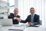 Two professionals shaking hands after a salary negotiation in an office