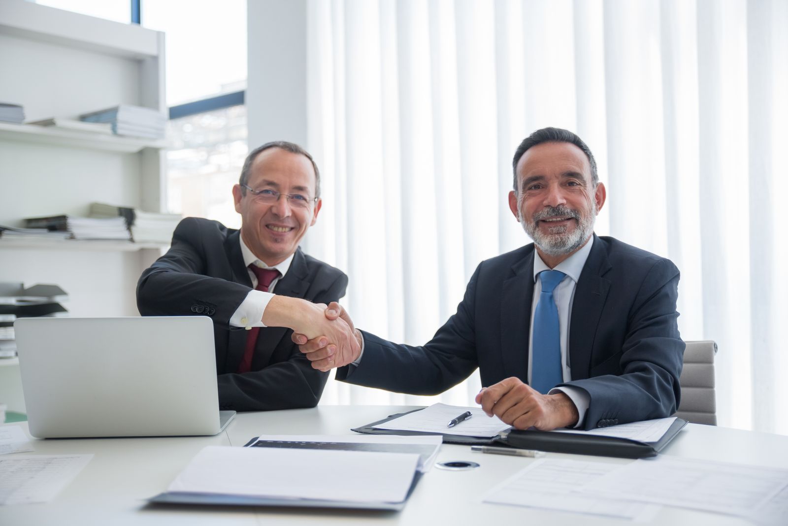 Two professionals shaking hands after a salary negotiation in an office
